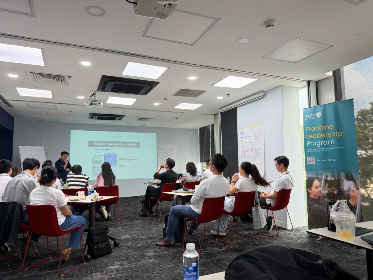 Participants in a Frontline Leadership Program session in Vietnam, with the ACOBI program banner beside the screen
